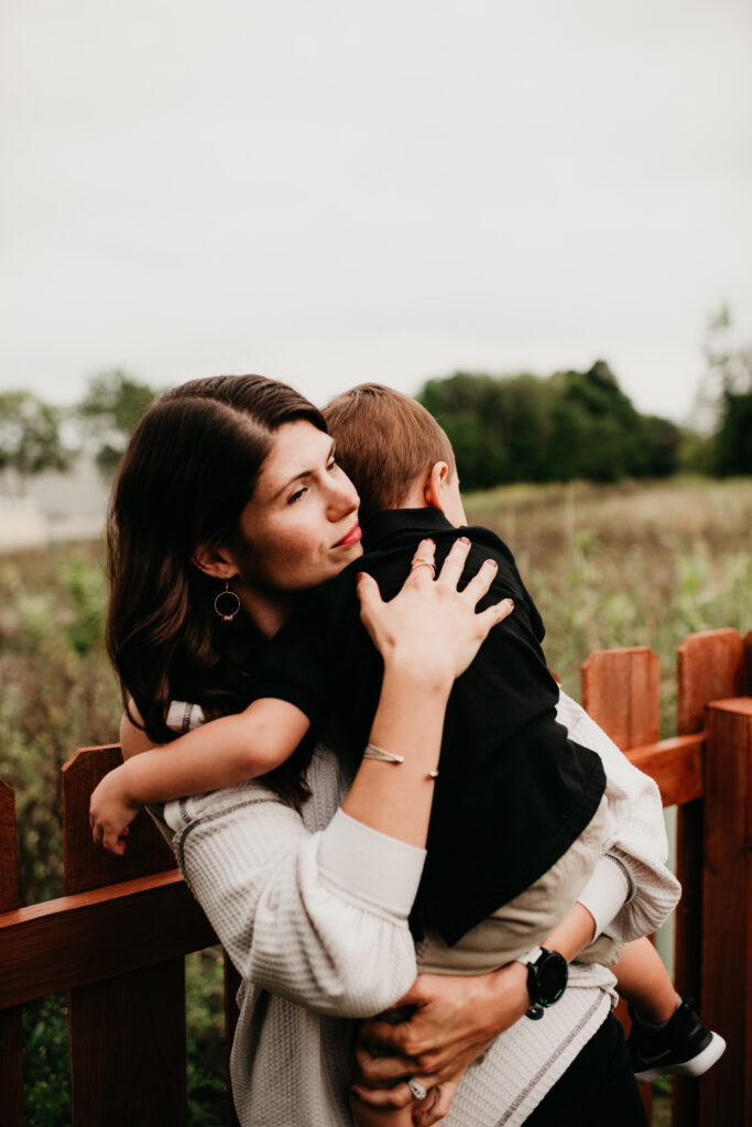 A mother holds her child close with a thoughtful expression, symbolizing the emotional strain and mental load of motherhood as she manages the unseen responsibilities of caregiving.