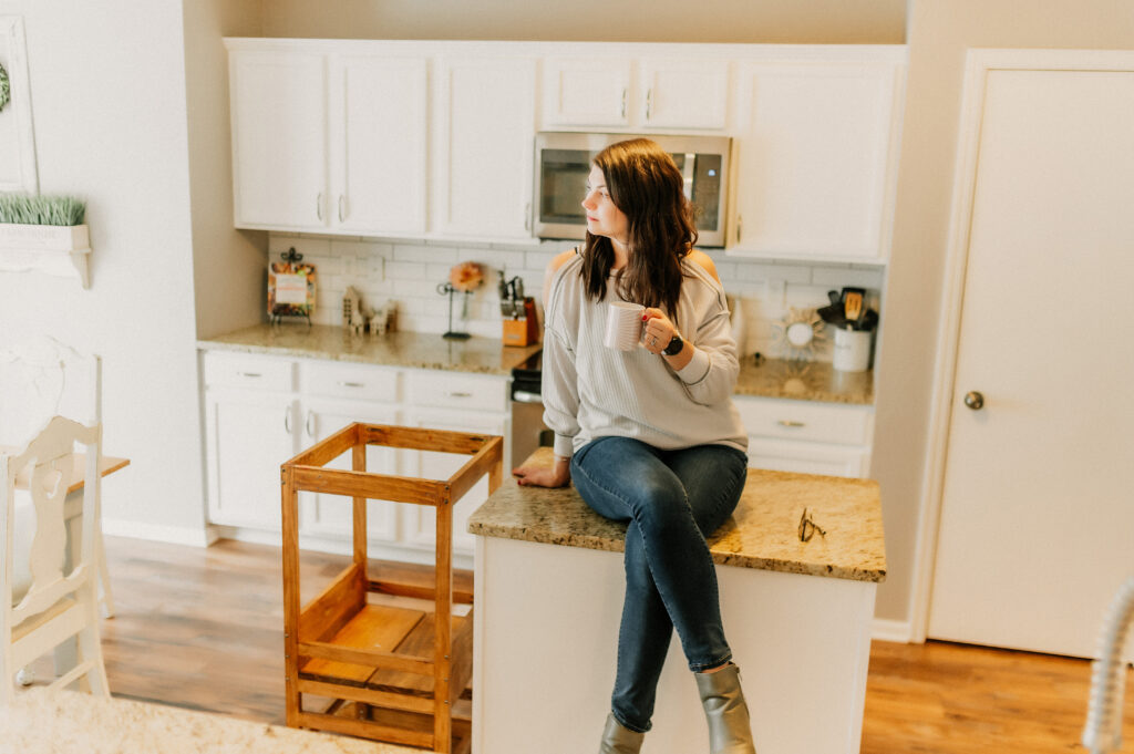 a women sitting on a kitchen island holding a cup 