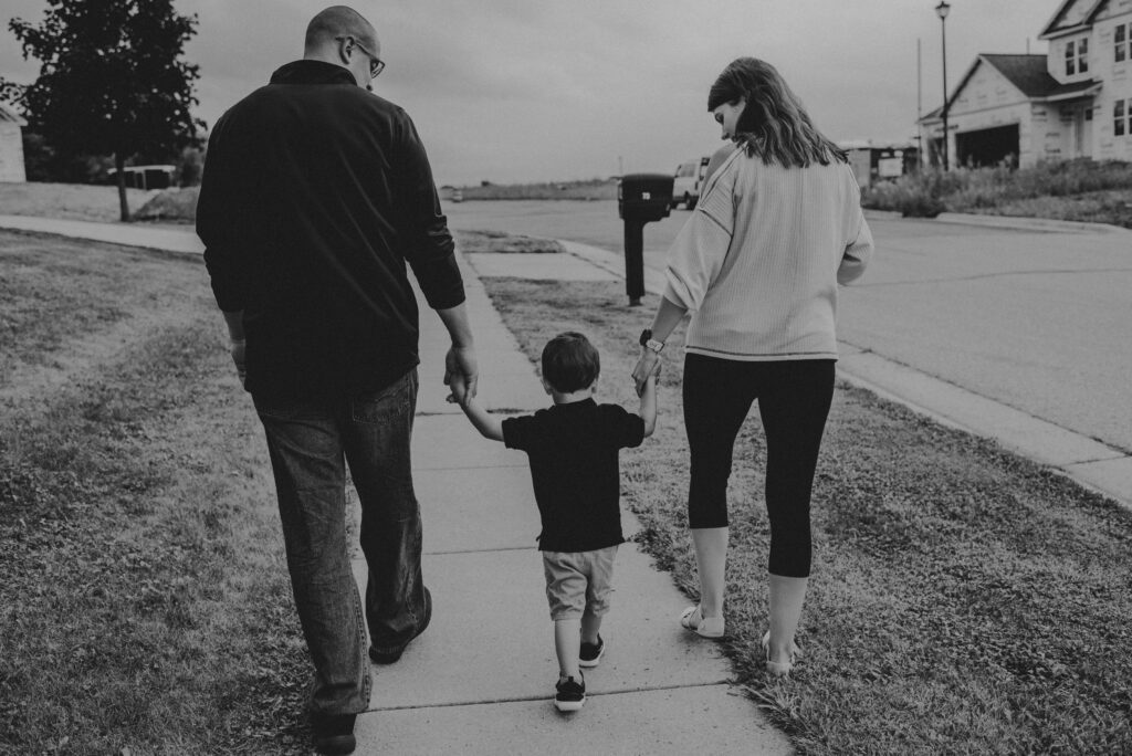 A mother, father, and child walk together hand in hand.