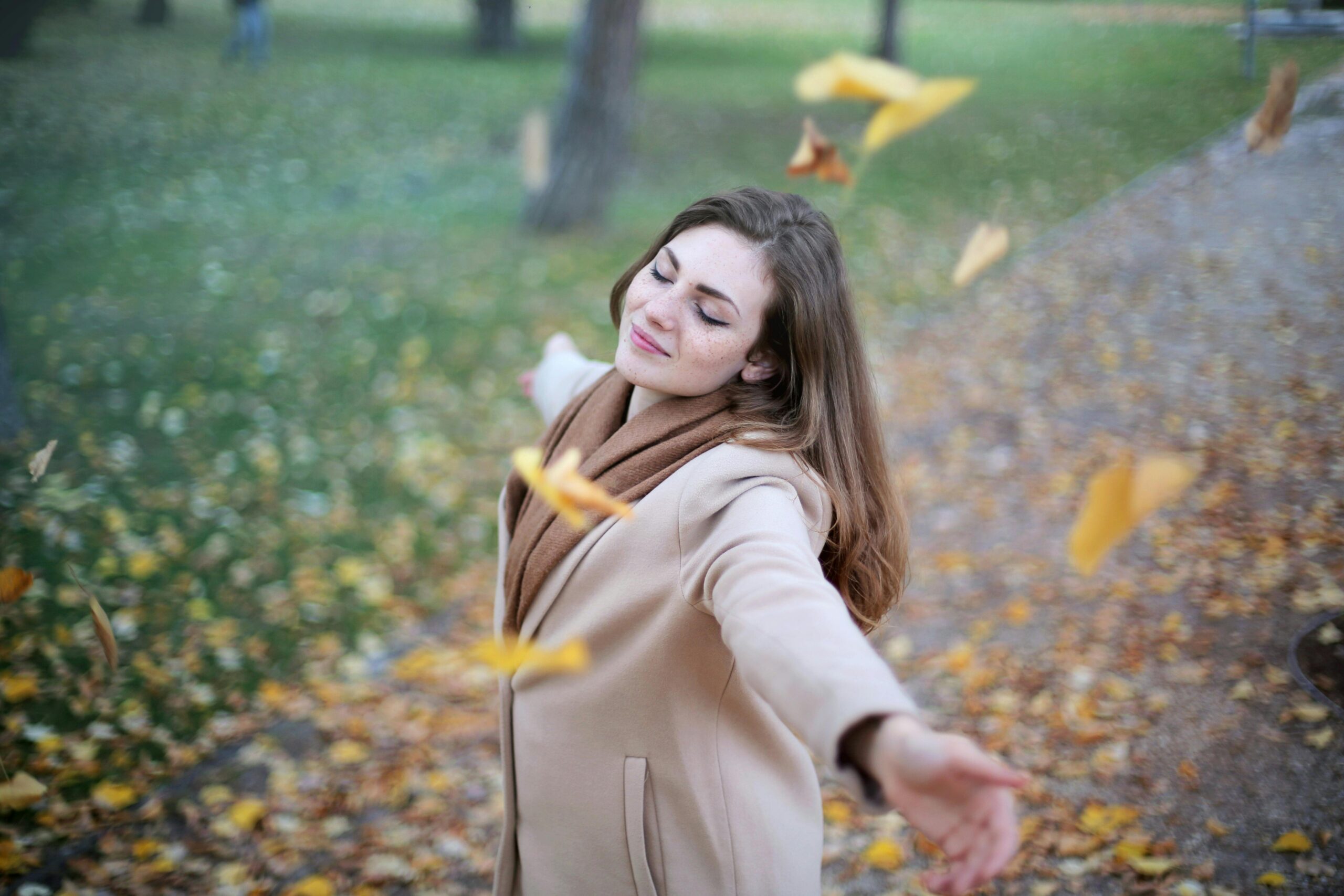 woman outside arms outstretched with leaves falling around her