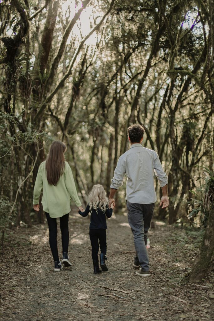 a mom, dad, and child holding eachothers hands in a walking trail with trees surrounding them | OCD in kids