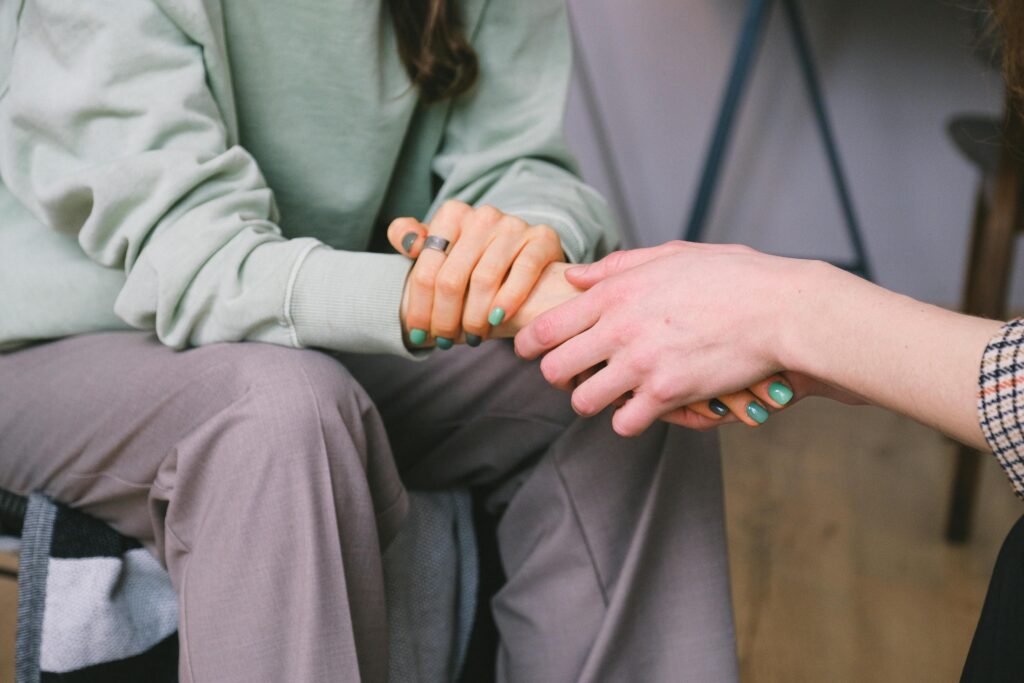 Two people sit together, holding hands in a supportive gesture. 