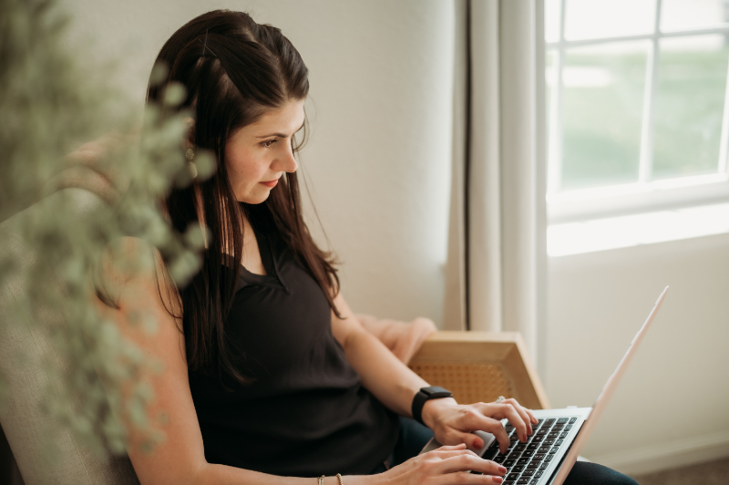 A woman uses a laptop near a window, balancing productivity and mindfulness as she explores how technology impacts mental health.