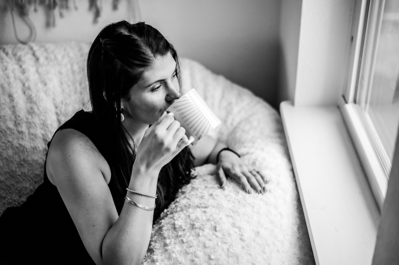 A black-and-white photo of a woman sipping coffee by a window.