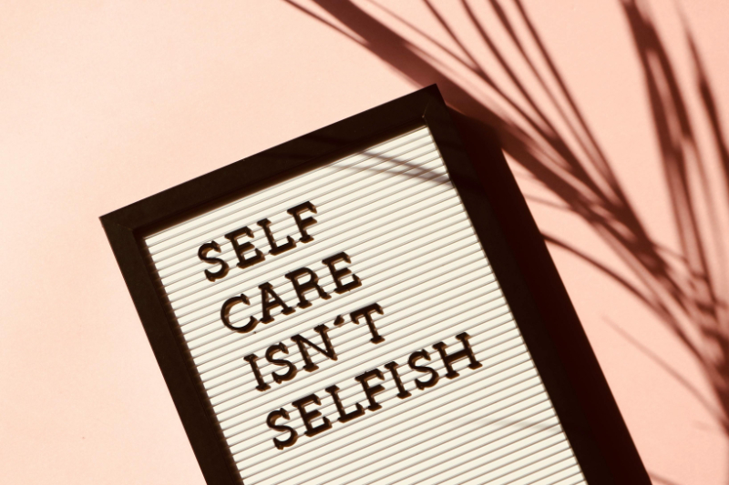 A letter board with the phrase "Self care isn't selfish" sits on a pink background with soft shadows.