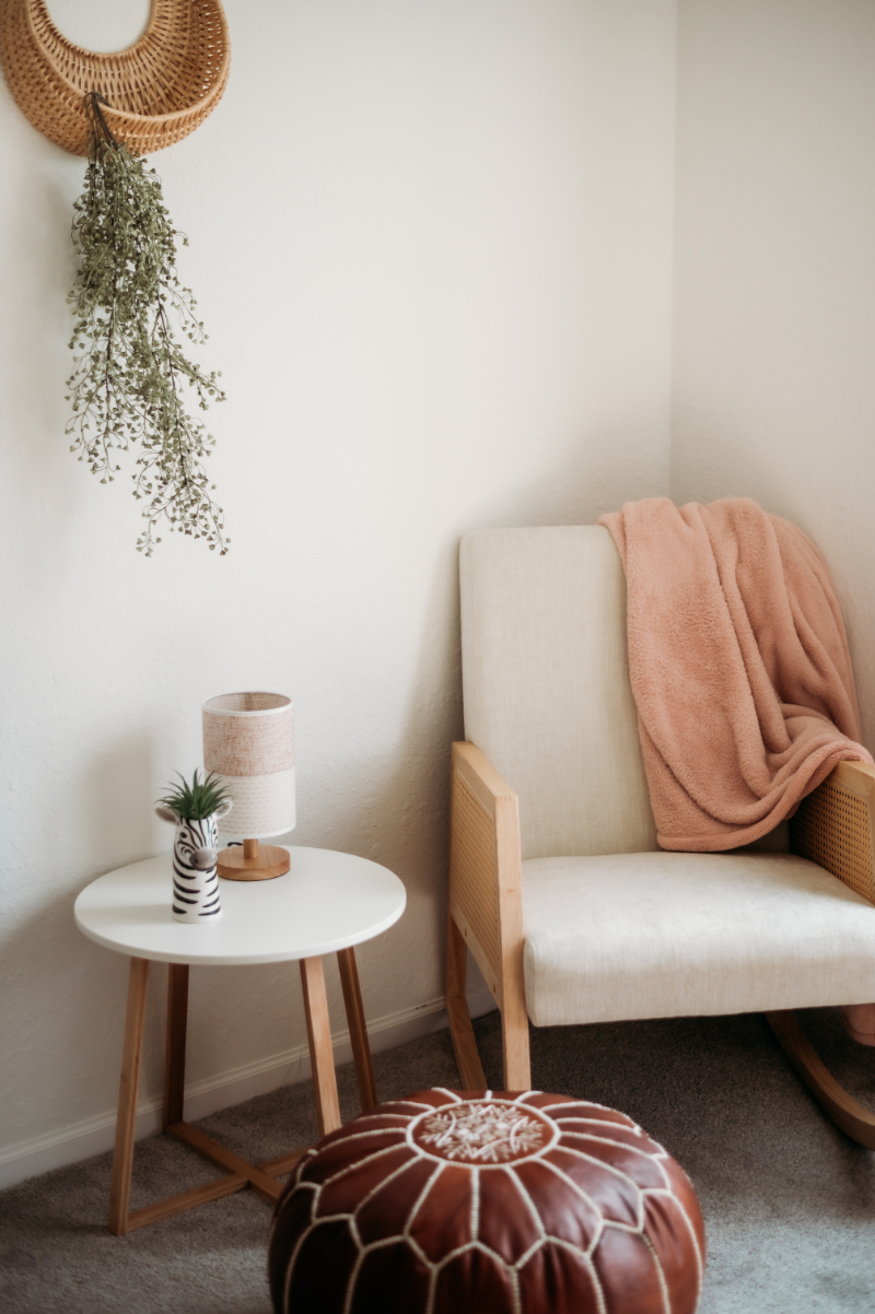 A serene corner with a rocking chair, soft blanket, side table with a zebra vase, and a pouf on the floor, evoking relaxation | self care isn't selfish