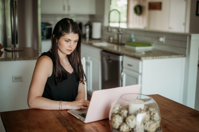 a person sitting on a kitchen table with a pink laptop.