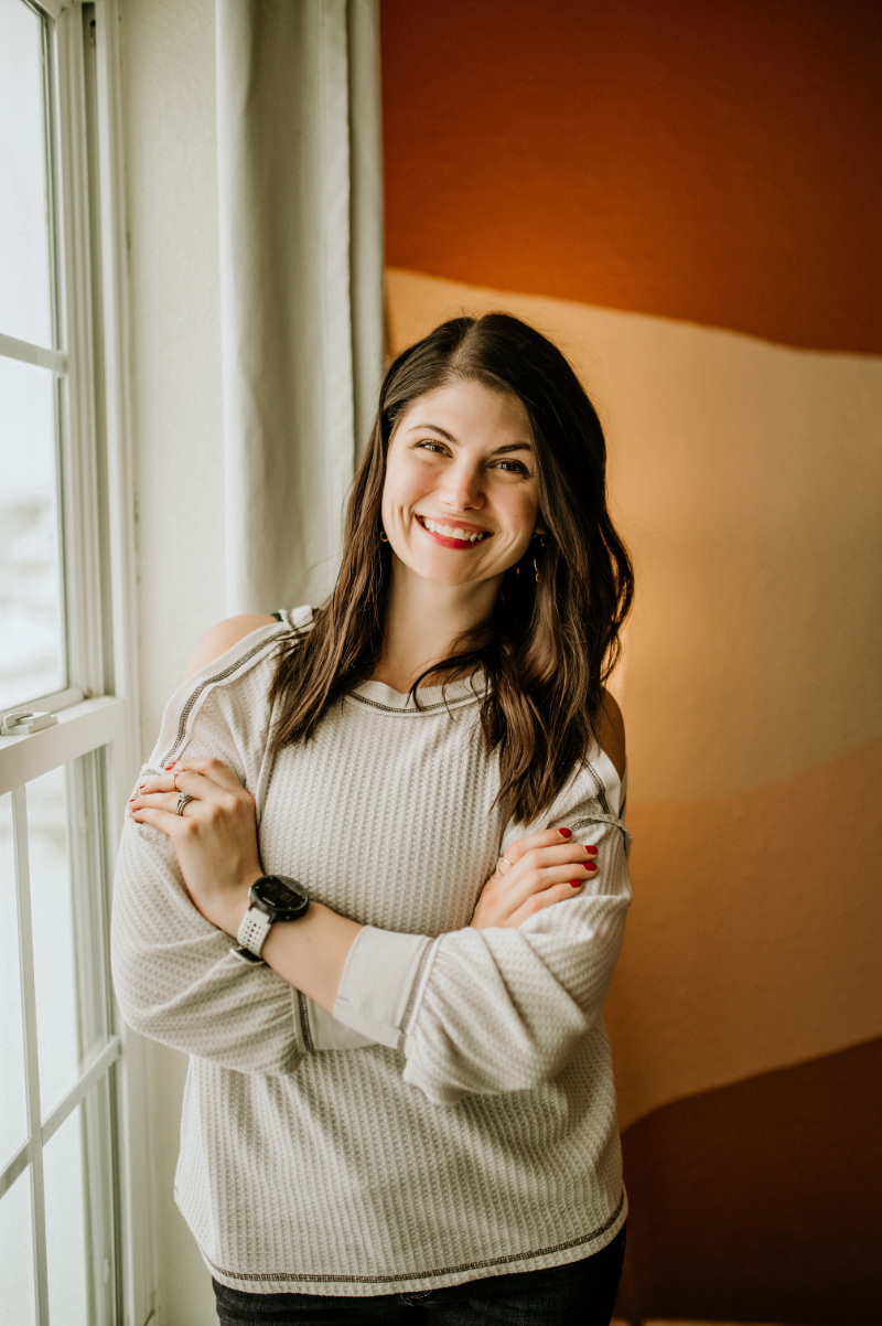 woman standing by a window arms crossed smiling at the camera | how to manage anxiety and OCD
