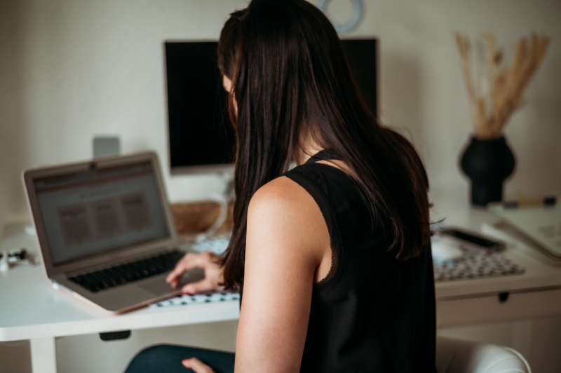 Woman works at a desk on a laptop, focused on her computer in a home office.