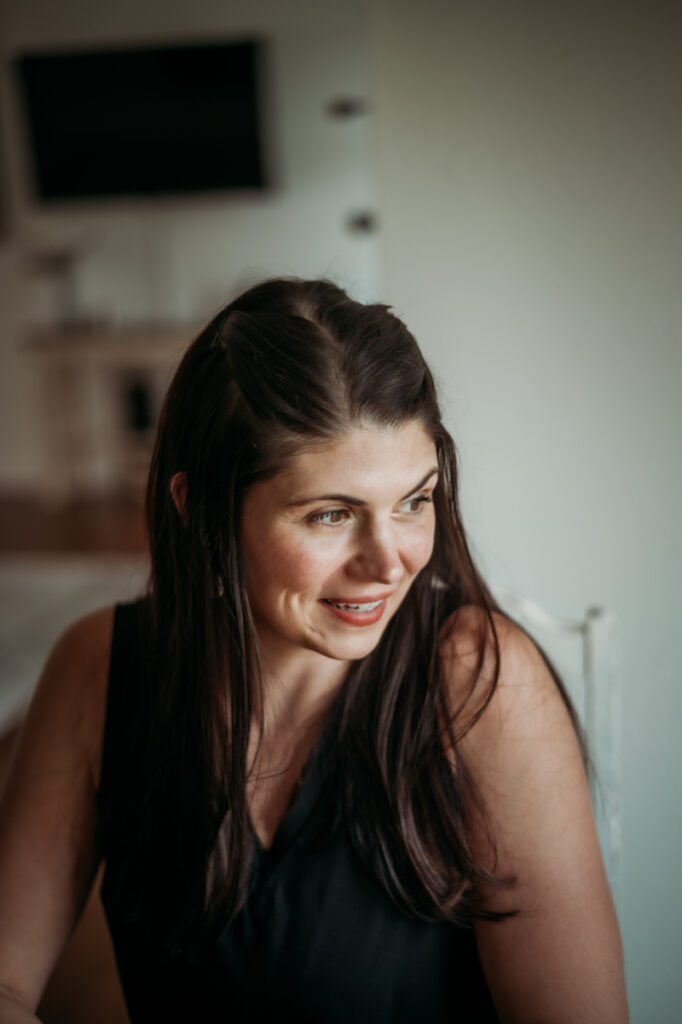 Woman smiles softly, looking to the side in a cozy indoor setting with warm lighting.