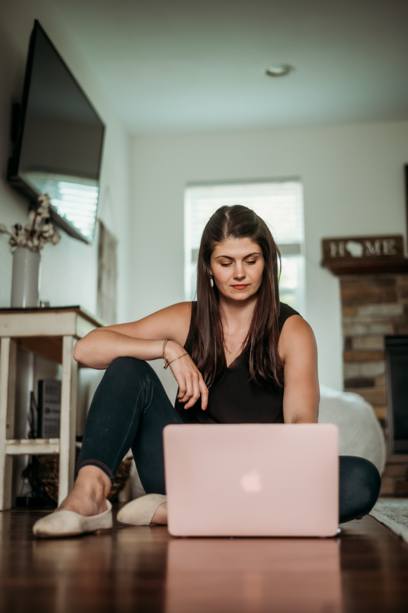 Woman sits on the floor working on a pink laptop, focused and relaxed in a bright living room.