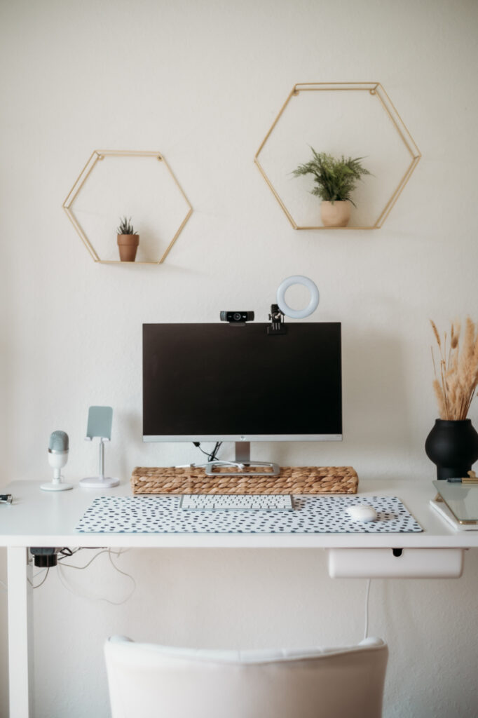 Minimalist workspace with monitor, microphone, keyboard, ring light, and simple wall decor.