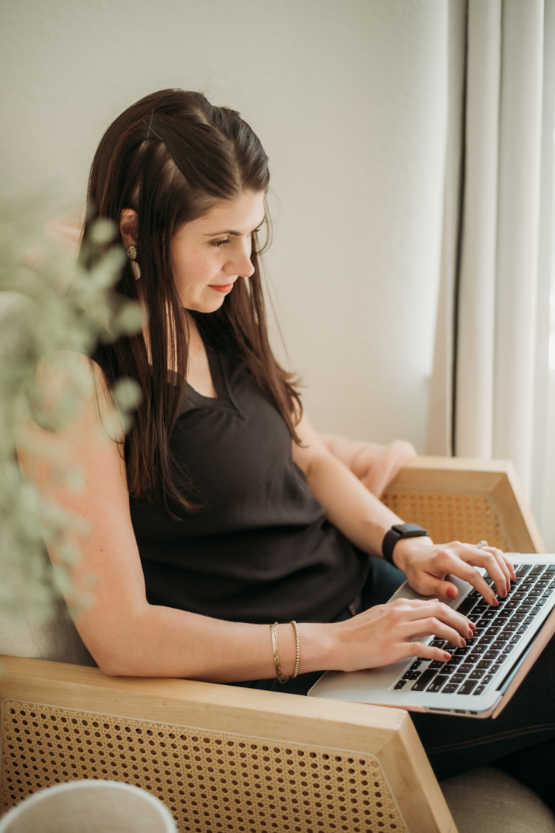 A woman types on her laptop while seated comfortably—focused on sharing parenting and mental health support.