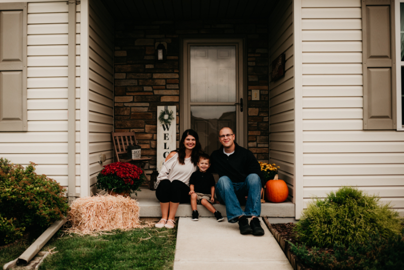 A family of three sits on their front porch, smiling—capturing a warm moment tied to parenting and mental health.