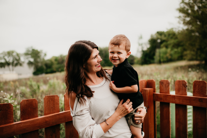 A smiling mom holds her young son outside by a wooden fence—soaking in a joyful moment during summer break while balancing OCD and parenting.