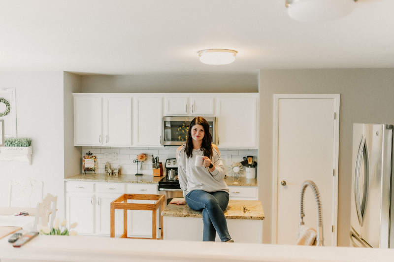 A woman sits on her kitchen counter sipping from a mug—finding a quiet, grounding moment during summer break while navigating the ups and downs of OCD.