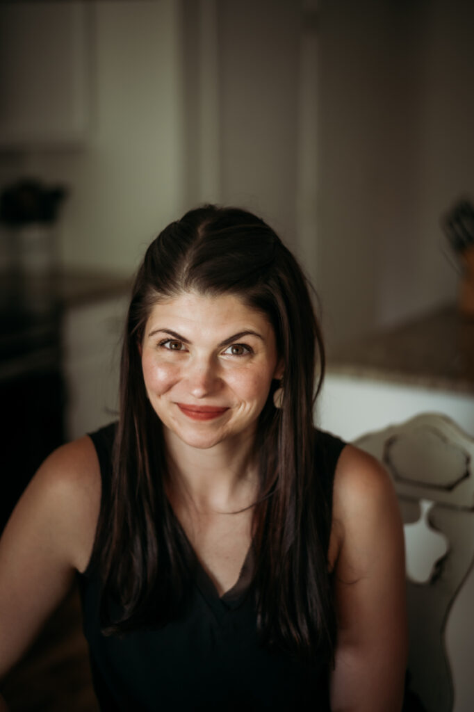 A woman sits at her kitchen table with a calm, confident expression—ready to help others talk about mental health and lead their families with empathy, strength, and truth.