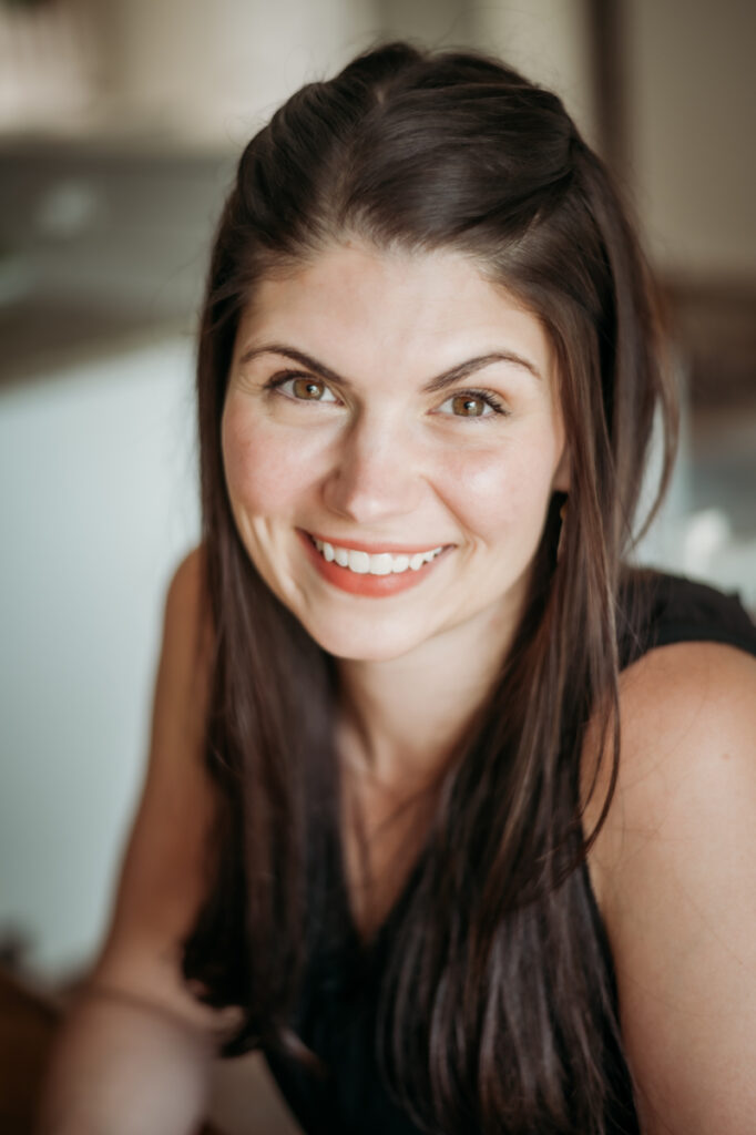 A close-up portrait of a woman smiling warmly at the camera, radiating a calm and welcoming energy.