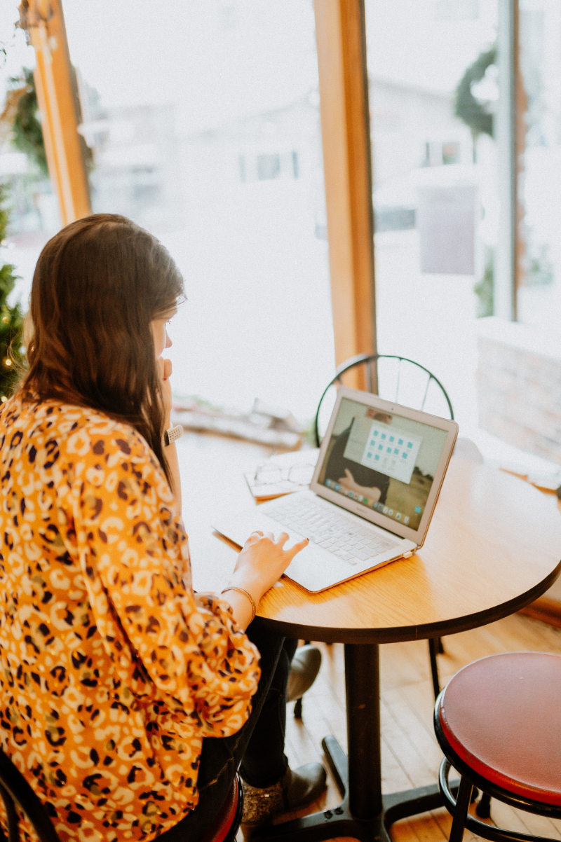 A woman sits at a cozy café table working on a laptop, focused and thoughtful—possibly organizing content or resources related to OCD support.